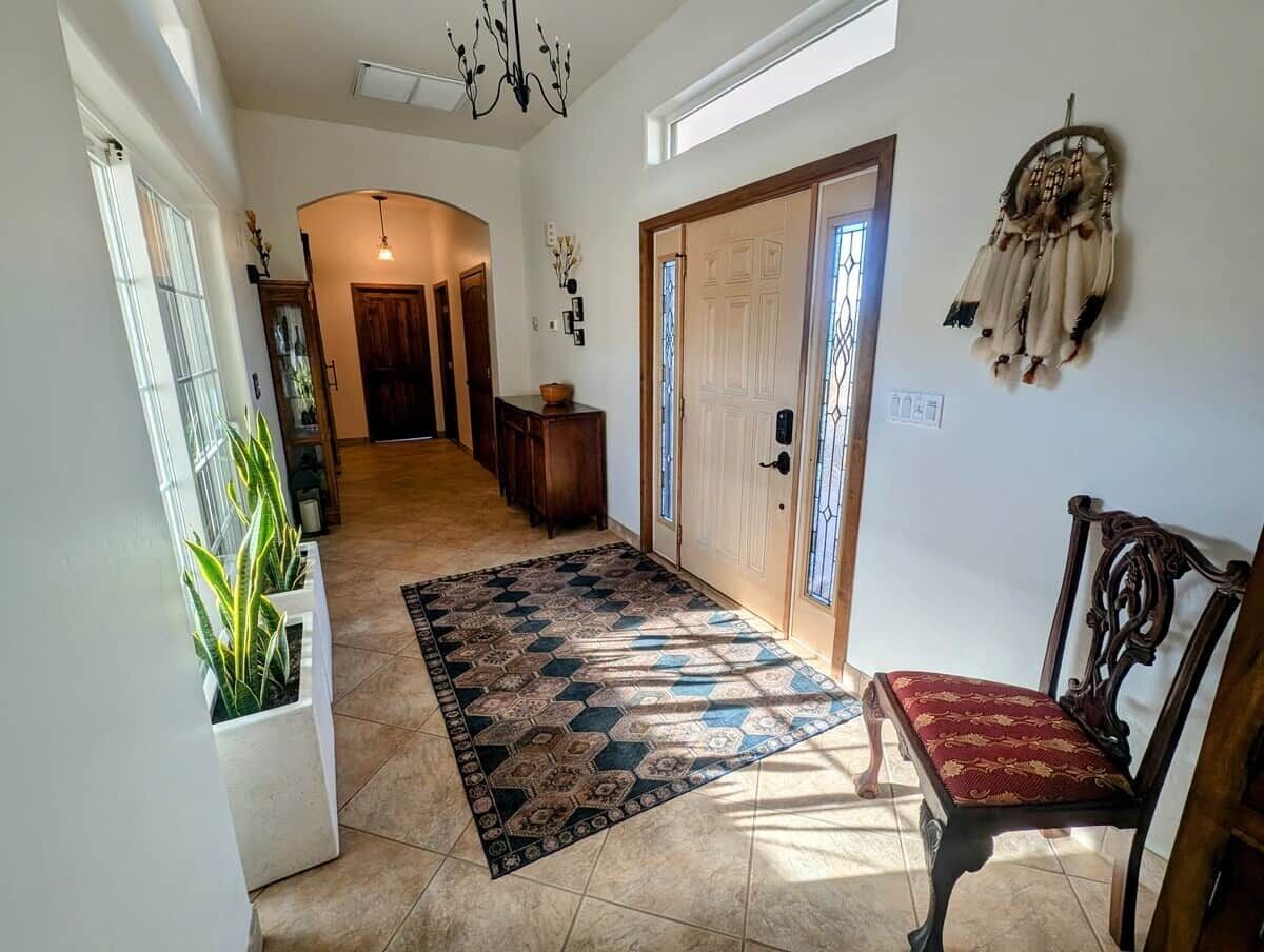 A hallway with a patterned rug, a wooden bench, a dreamcatcher, and a door with a window.