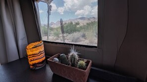 A window with a view of a mountainous landscape, a textured lamp, and a terracotta pot with cacti.