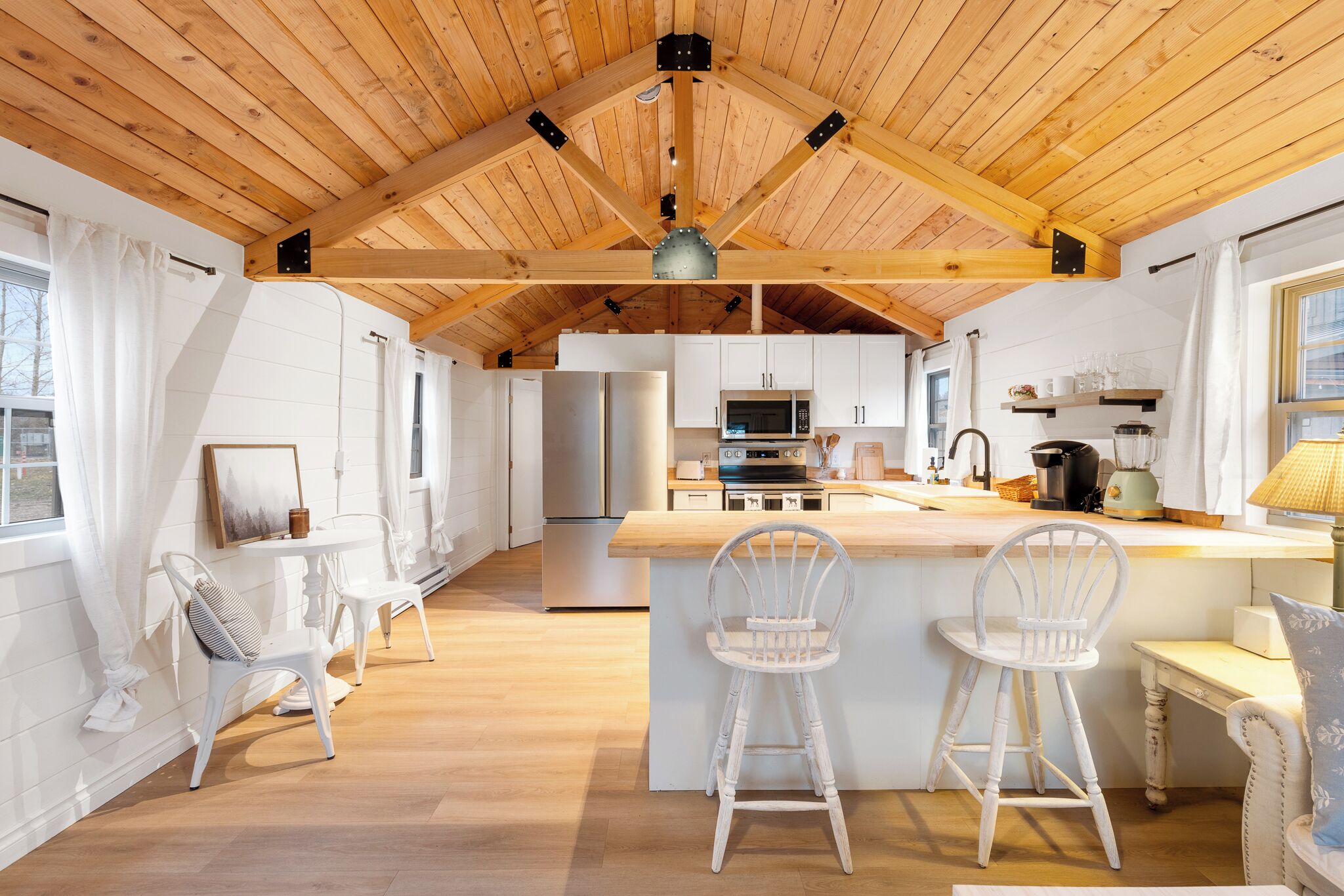 A spacious kitchen with wooden beams, white cabinetry, and a central island with bar stools.