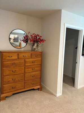 A wooden dresser with multiple drawers, a round mirror, and a vase with red flowers on top.