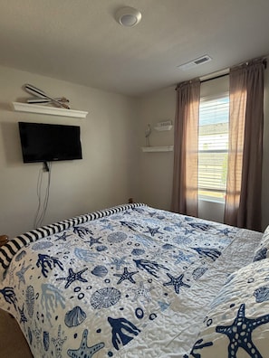 A bedroom with a bed, a mounted television, a window with curtains, and a shelf with a remote control. - Welcome to Your Pacific Northwest Retreat (Vancouver)