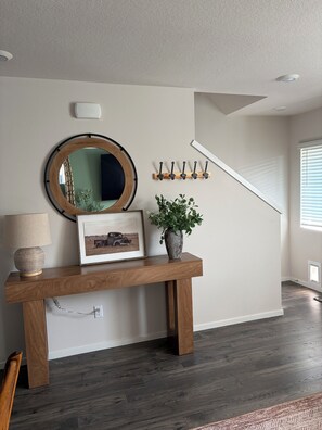 A hallway with a wooden console table, a round mirror, a framed picture, a potted plant, a coat rack, and a staircase.