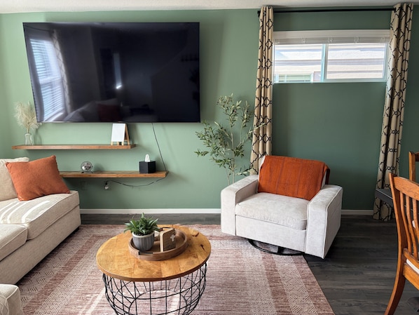 A living room with a flat-screen TV, two sofas, a coffee table, and a window with patterned curtains.