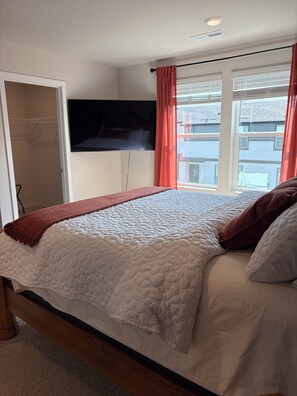 Un dormitorio con una cama, un televisor montado en la pared, una ventana con cortinas y un armario.