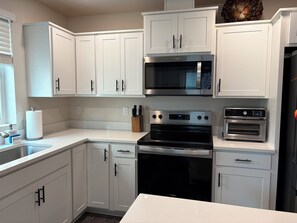 A modern kitchen with white cabinetry, a stainless steel microwave, a built-in oven, and a countertop with a soap dispenser and sponge. - Welcome to Your Pacific Northwest Retreat (Vancouver)