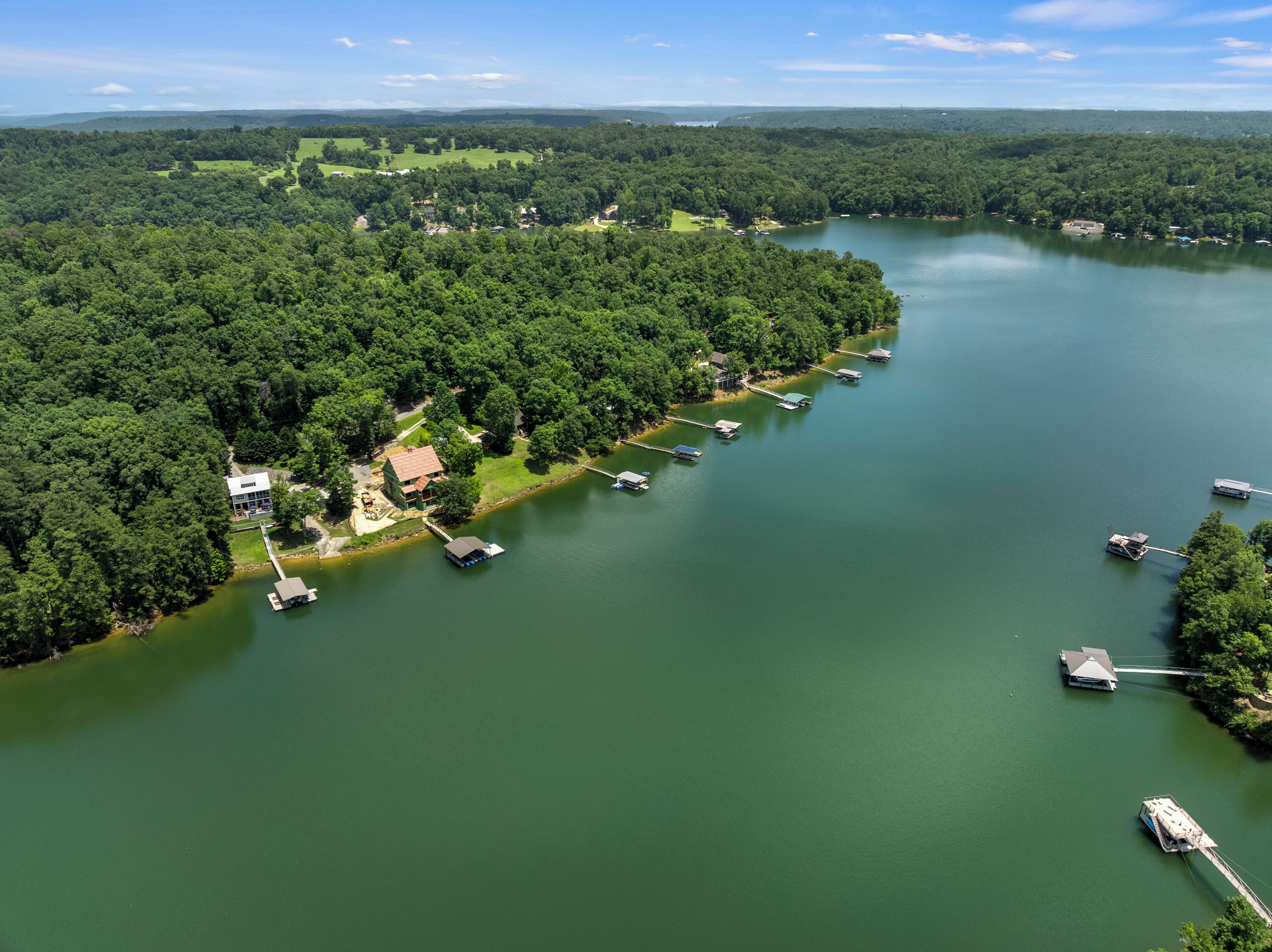 Vue aérienne d’une propriété au bord du lac, avec des bateaux amarrés, une maison et la forêt environnante.
