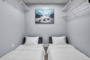 Une chambre avec deux lits, un tableau représentant des bateaux sur l’eau et un étendoir fixé au plafond.