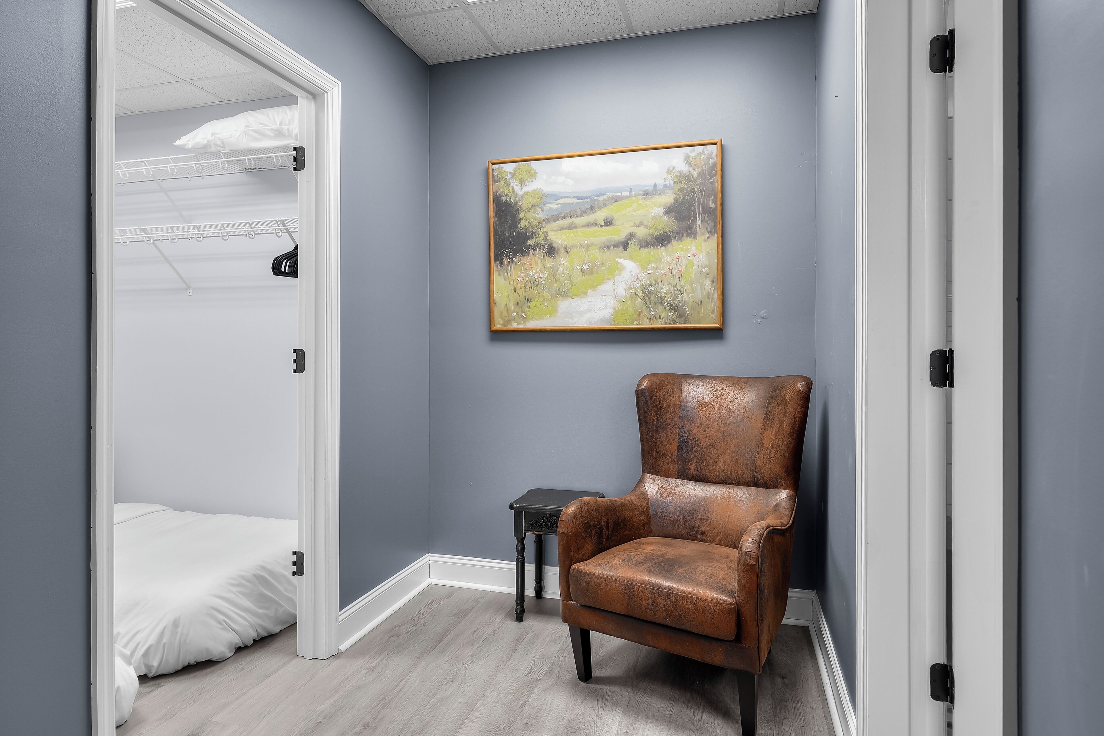 Une pièce avec un lit superposé, une chaise, une petite table et un tableau représentant un paysage accroché au mur.