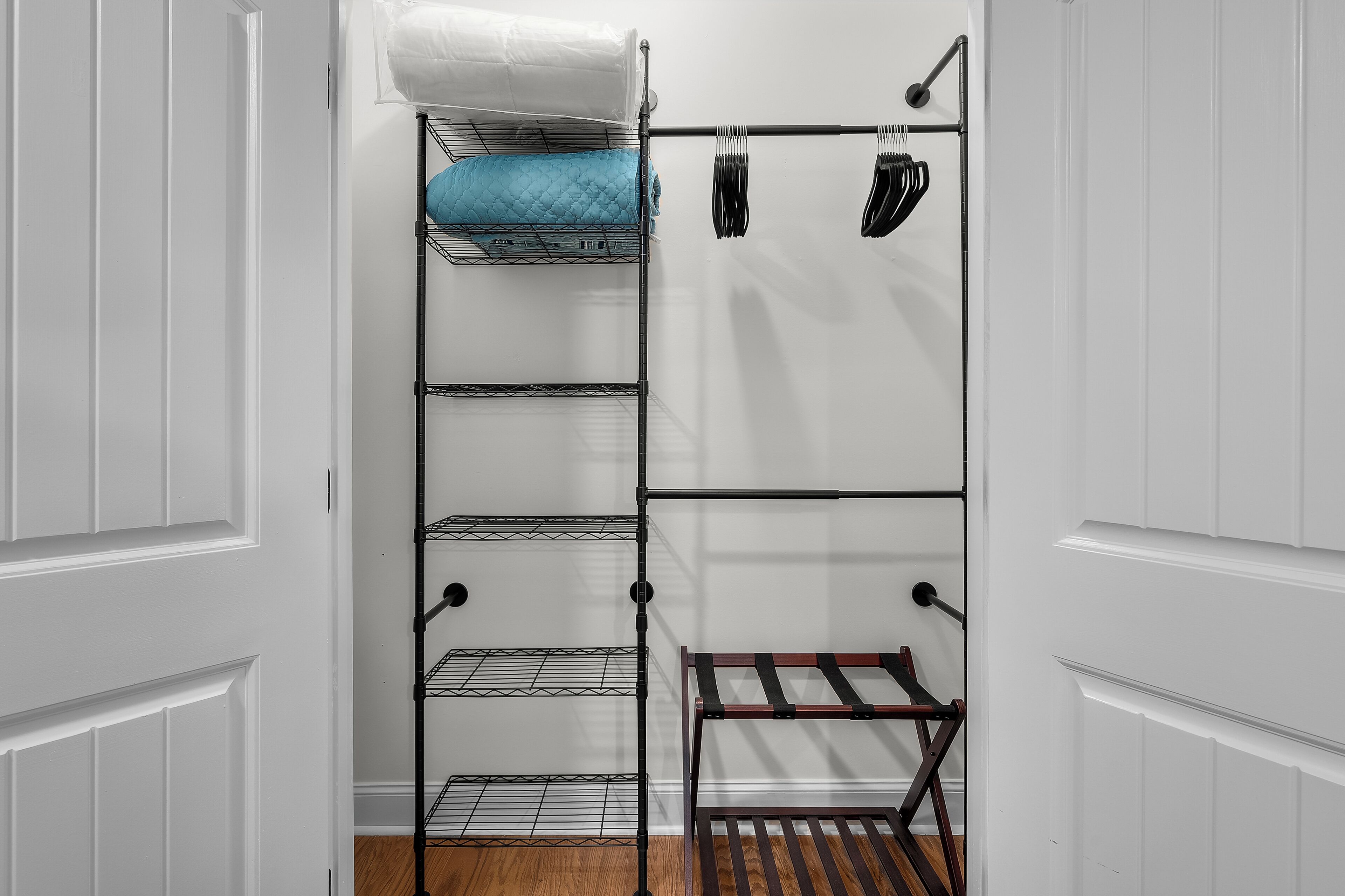 A white closet with a metal shelving unit, a wooden bench, and a hanging rack with clothes.