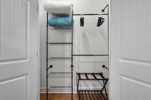 A white closet with a metal shelving unit, a wooden bench, and a hanging rack with clothes. - Gather at Smith Lake | Boat Ramp | Sleeps up to 10 | Crane Hill lakefront home (Crane Hill)