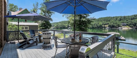 A deck with outdoor furniture and umbrellas overlooking a lake.