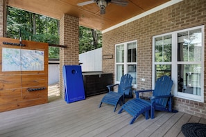 Un porche techado con terraza de madera, un panel informativo con mapa, una parrilla y sillas Adirondack azules.
