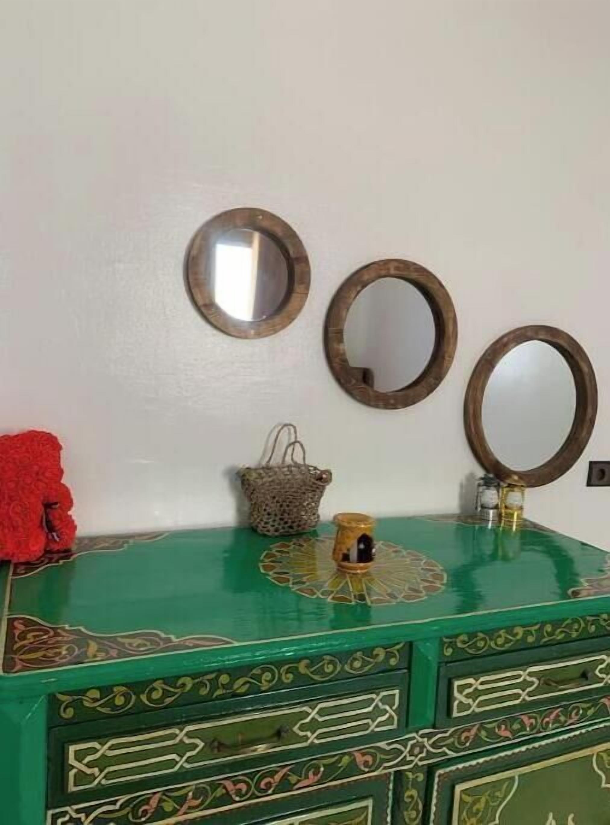 Une commode verte avec trois miroirs et un petit objet décoratif posé sur le dessus.