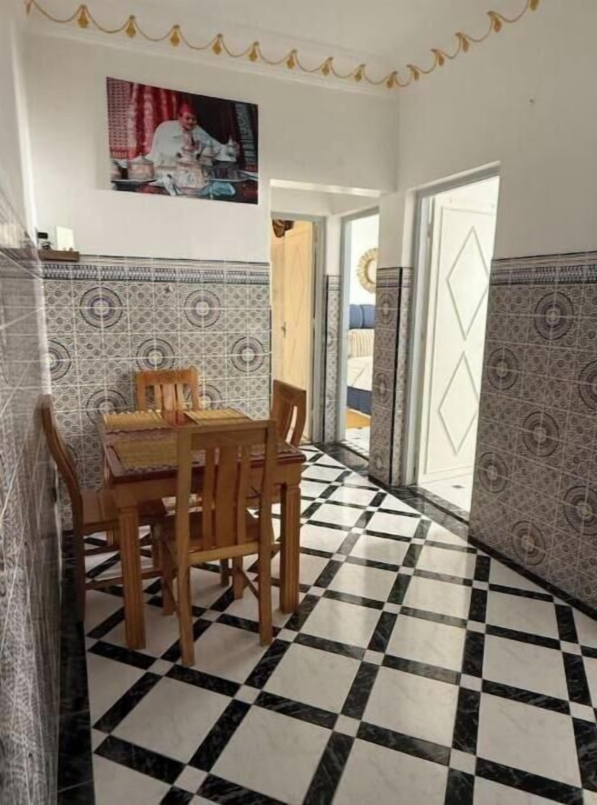 Een eetgedeelte met een zwart-wit geruite vloer, behang met patroon en een houten tafel met stoelen.