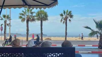 Uitzicht op een strand met palmbomen, een zandstrand en een weg met voertuigen.
