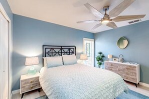 A bedroom with a bed, nightstands, a dresser, a ceiling fan, and a window with blinds. - Purple Pelican Cottage | Old Florida island escape (Naples)