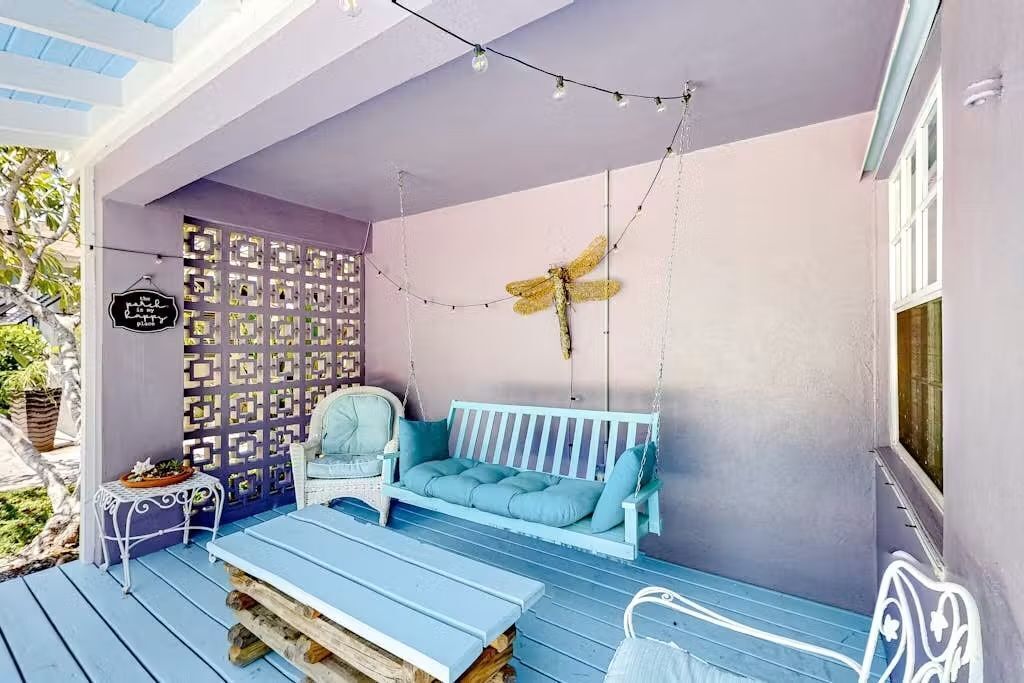 A porch with a swing, a bench, a decorative wall, and a hanging dragonfly.