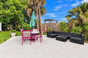 Een terras buiten met een ronde tafel, stoelen en een zithoek.