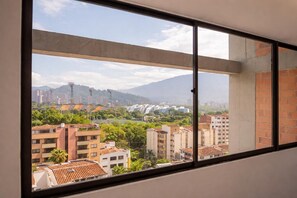 A room with a large window overlooking a cityscape with buildings and greenery. - Laureles Loft - View of the Stadium - 5-minute walk to the Metro (Medellín)