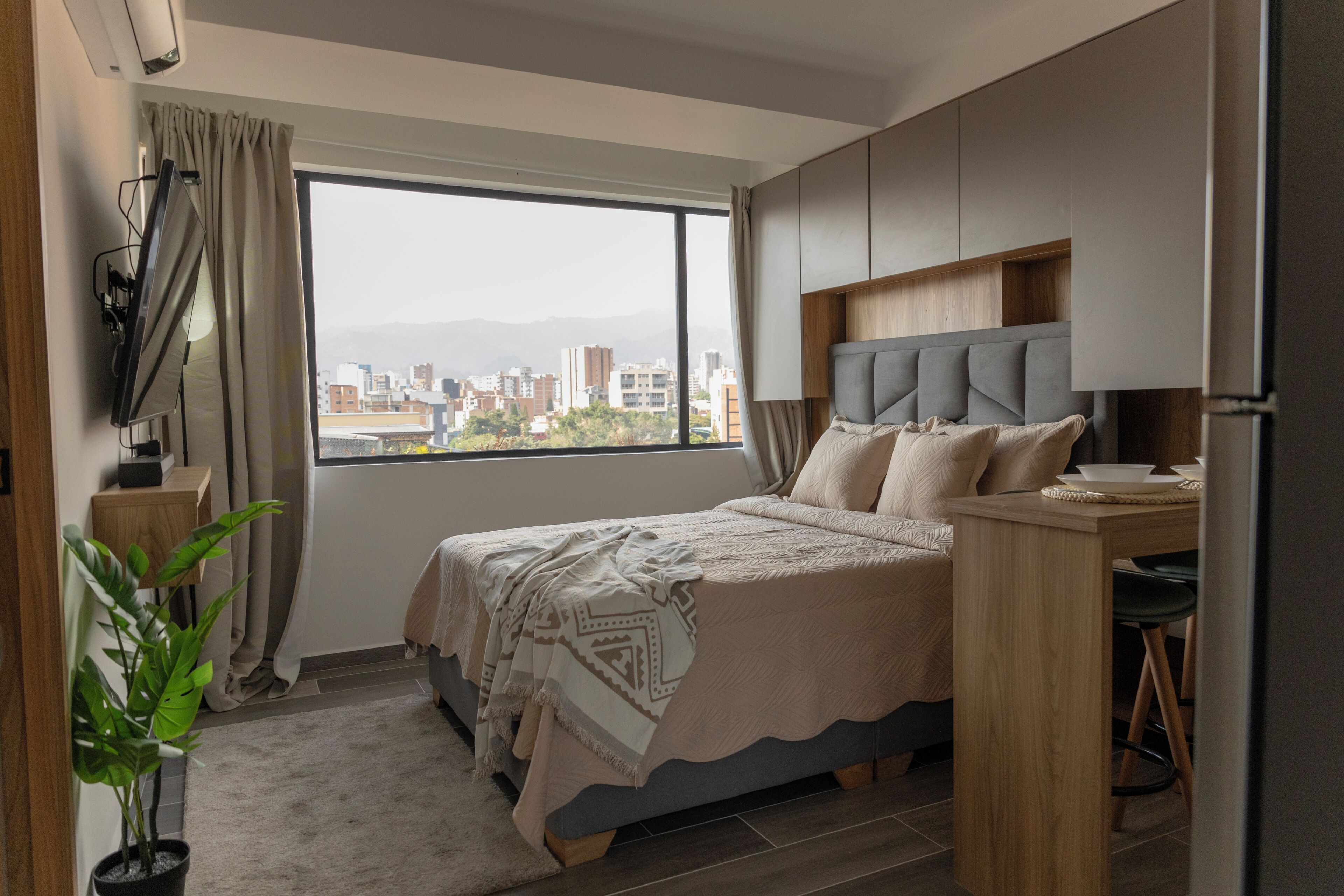 A modern bedroom with a bed, a desk, and a view of a cityscape.
