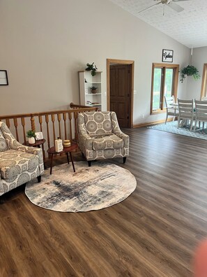 A living room with a wooden floor, patterned armchairs, a round rug, and a bookshelf.