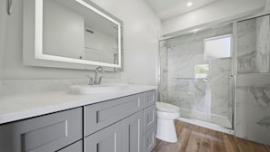 A modern bathroom with a marble sink, a large mirror, a toilet, and a glass-enclosed shower.