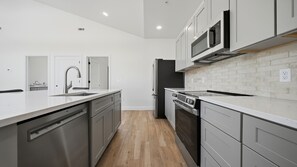 A modern kitchen with stainless steel appliances, white cabinetry, and a wooden floor.