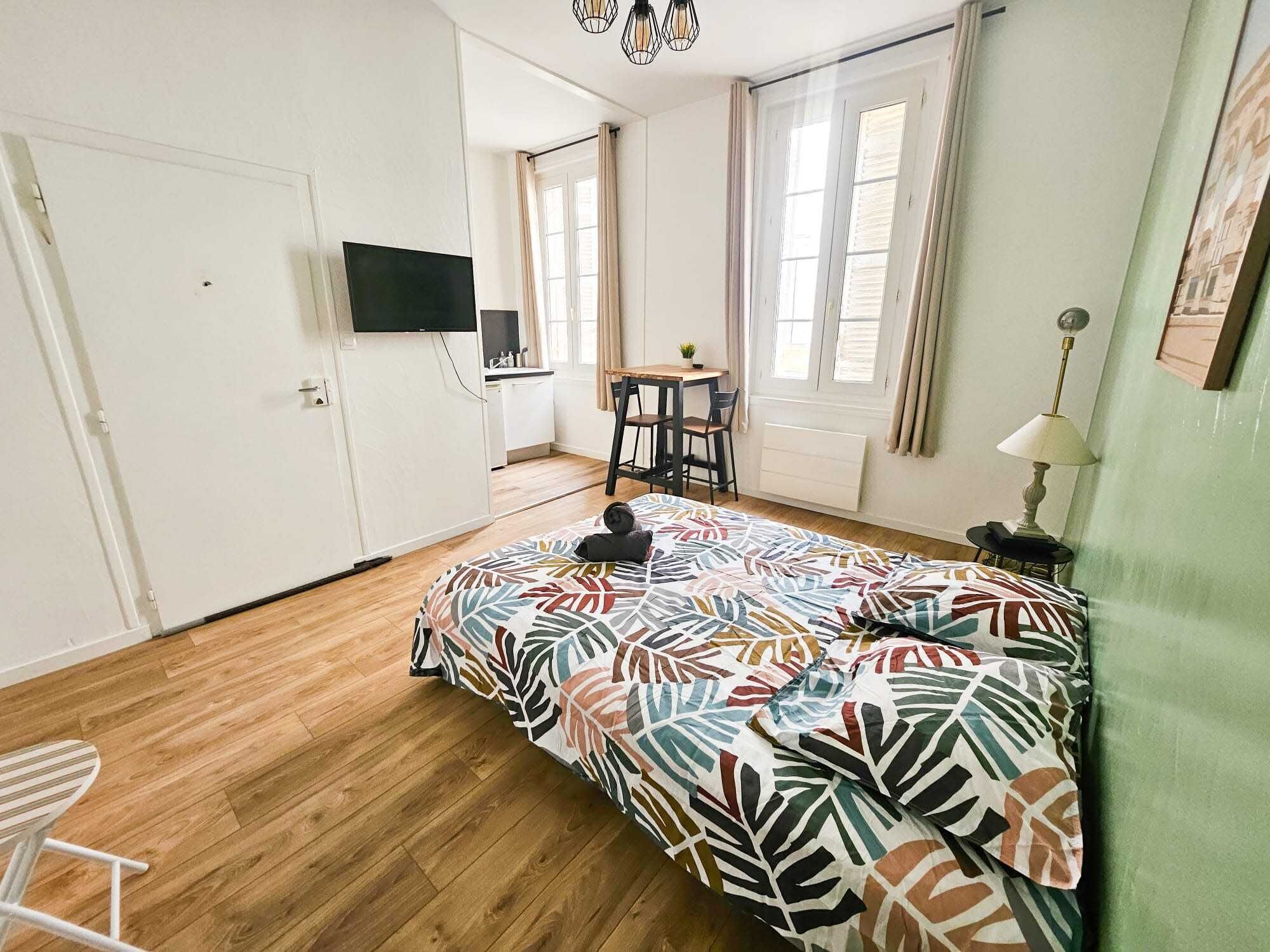 Ein Schlafzimmer mit einem Bett, einem Schreibtisch, einem Stuhl, einem Fernseher und einem Fenster mit Vorhängen.