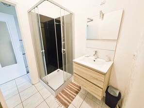 A bathroom with a glass shower enclosure, a white sink, and a mirror above it. - "Les Arches 1" City Center Studio (Saintes)