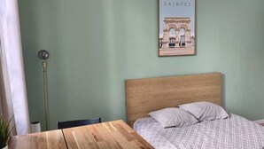 Una habitación con una mesa de madera, una cama con ropa de cama estampada, un cuadro en la pared y una lámpara en el techo.