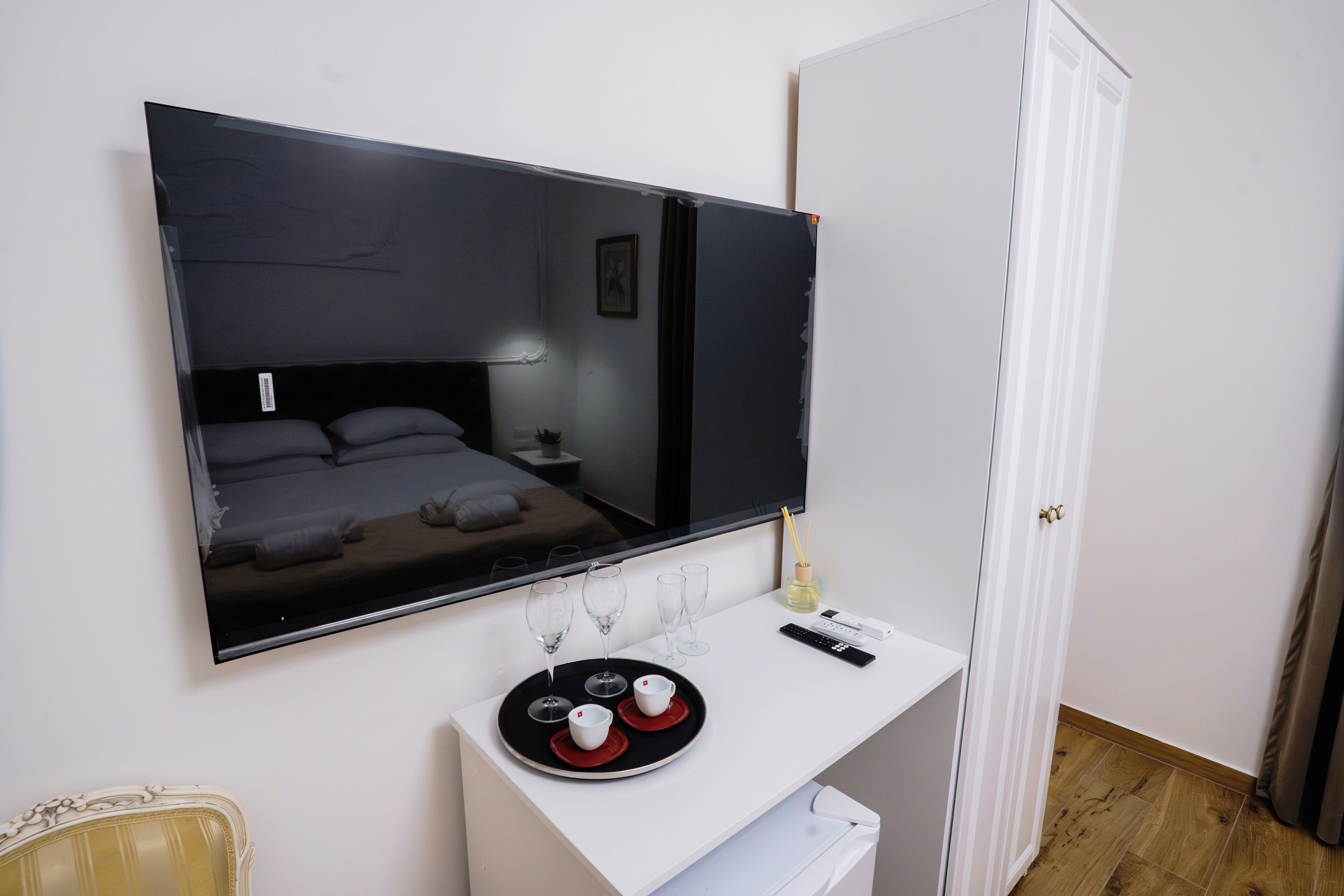 Een hotelkamer met een grote spiegel, een nachtkastje met een dienblad glazen en kopjes, een afstandsbediening, en een deur.