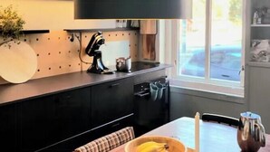 Una cucina moderna con una lampada a sospensione, un tavolo di legno con una ciotola di frutta e una finestra che si affaccia all'esterno.