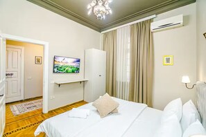 Ein Hotelzimmer mit einem Bett, einem Fernseher, einer Klimaanlage und einer Tür zu einem weiteren Raum.