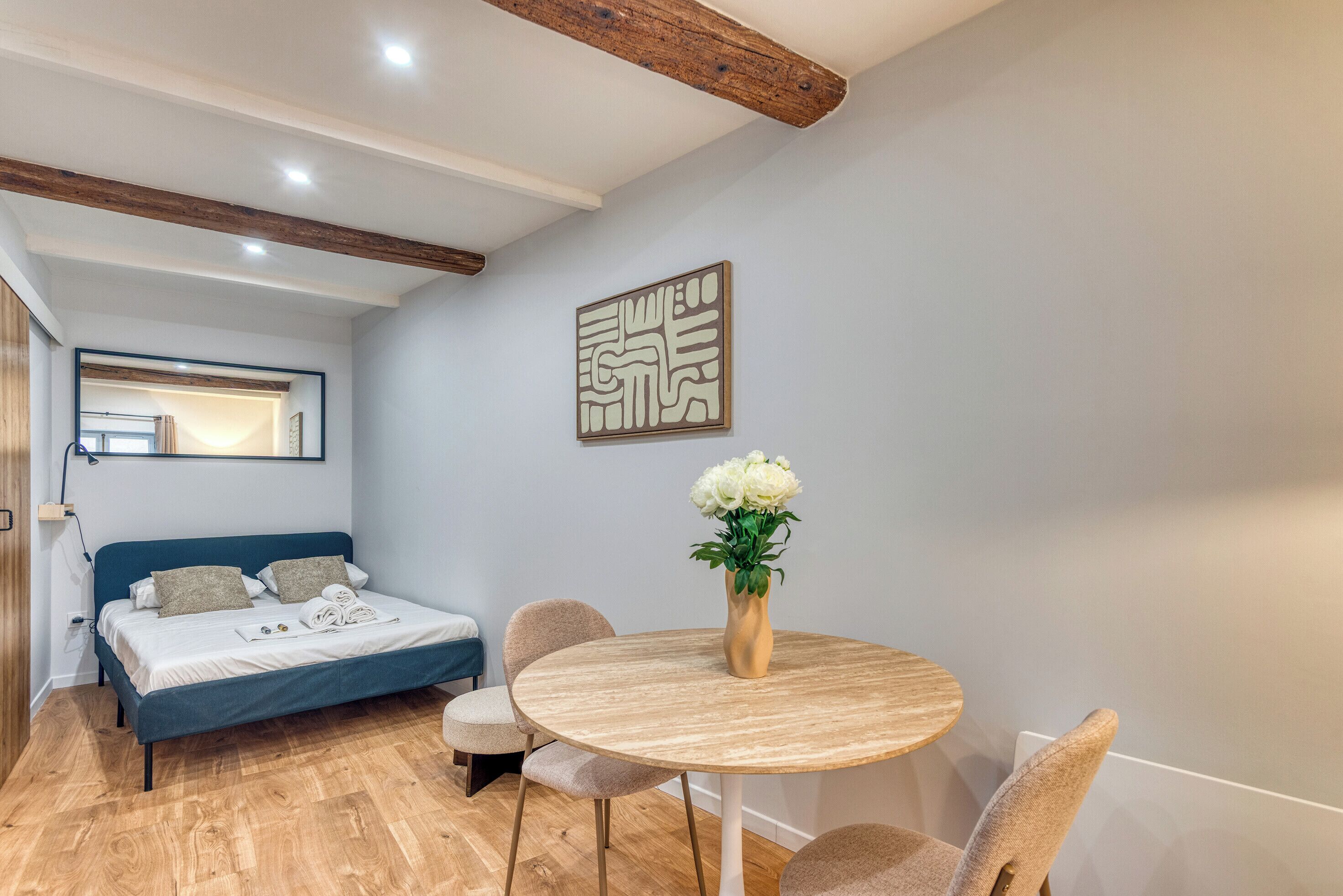 A bedroom with a bed, bedside table, and a round wooden table with chairs.