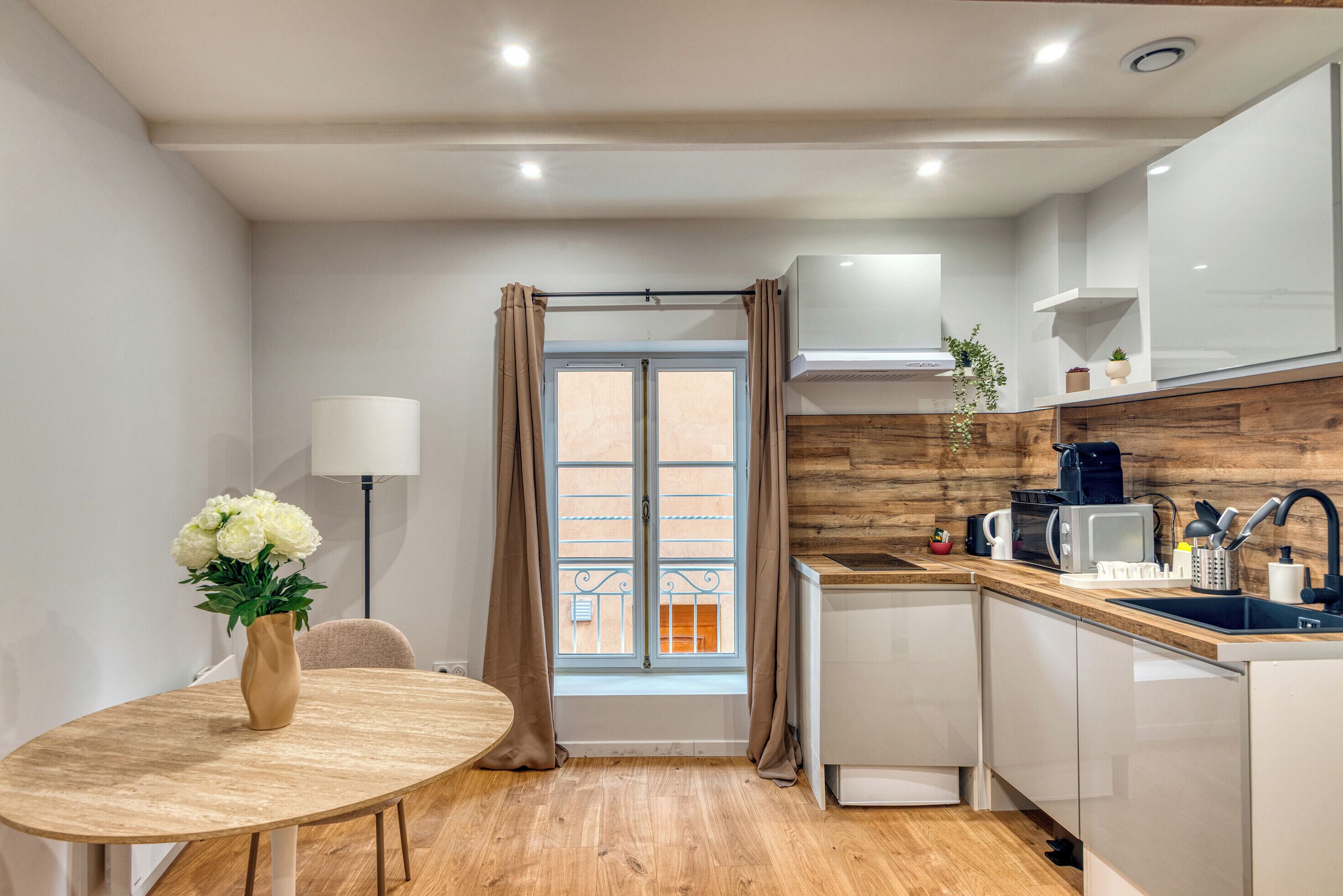 Uma cozinha moderna com área de refeições, piso de madeira e uma janela com cortinas.
