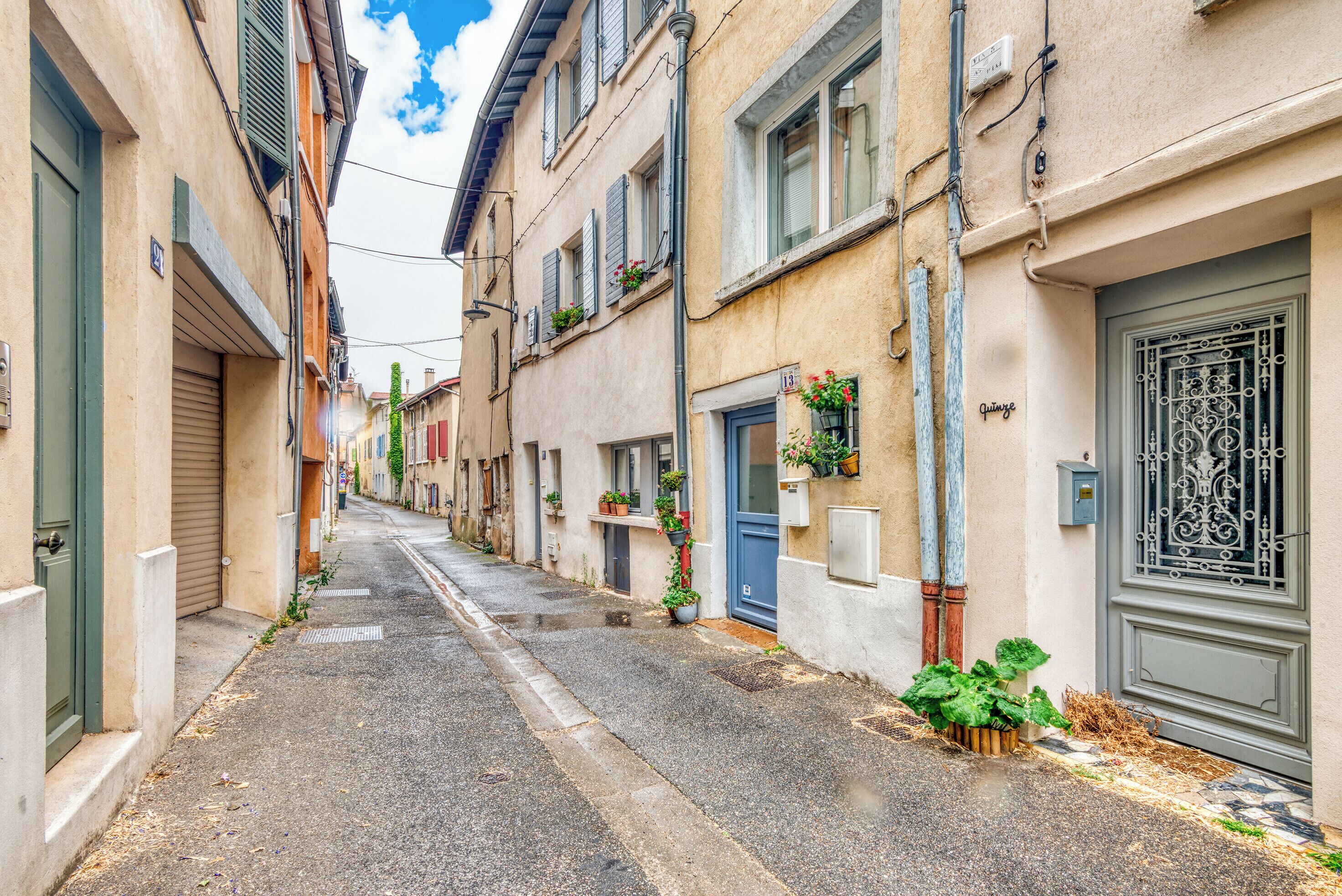 A narrow street with buildings on either side, some with shutters, and a few with flower boxes.