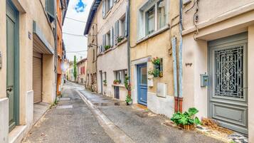 A narrow street with buildings on either side, some with shutters, and a few with flower boxes.