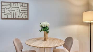 A dining area with a round table, four chairs, a vase with flowers, and a wall-mounted abstract art piece.