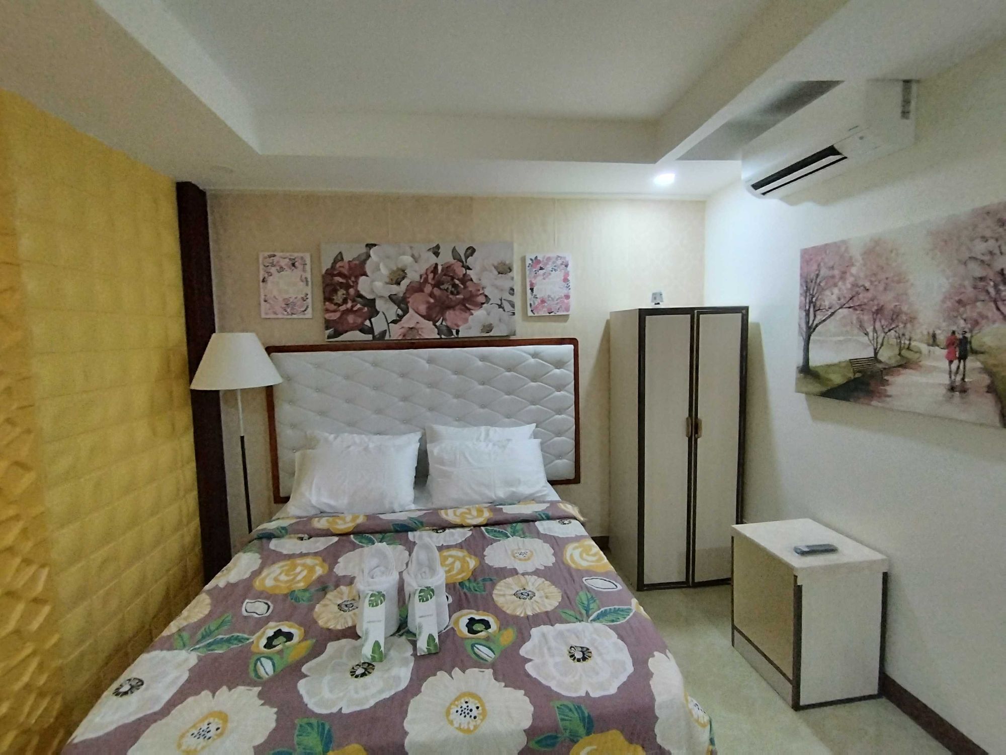 A hotel room with a bed, a bedside table, a wardrobe, and a painting on the wall.