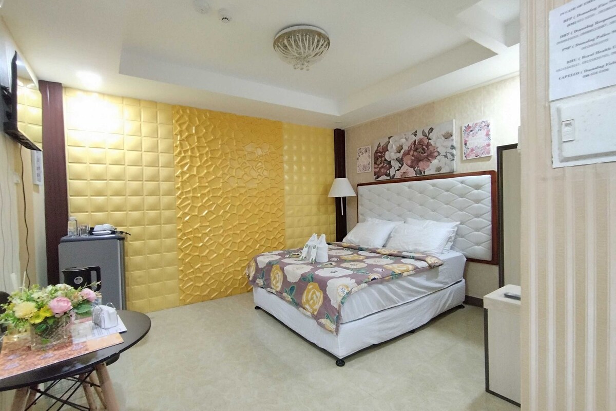 A hotel room with a bed, a desk, a chair, and a small table with a vase of flowers.