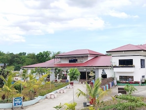 A two-story building with a red roof, surrounded by greenery and potted plants. - Donya Thelma Ferrer Spring Resort (Dumalag)