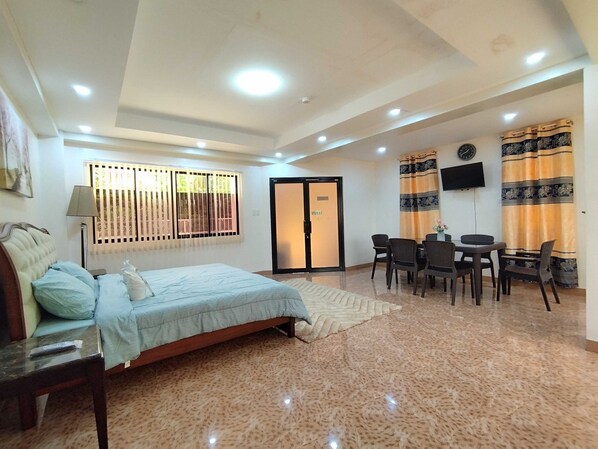 A hotel room with a bed, a desk, chairs, a television, and a window with blinds.
