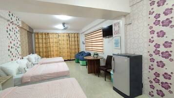 A hotel room with two beds, a small table, a chair, a television, and a refrigerator.