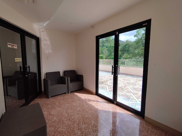 A room with two chairs, a small table, and a sliding glass door leading to an outdoor area with a patterned floor. - Donya Thelma Ferrer Spring Resort (Dumalag)