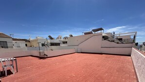 Una terraza en la azotea con tejas rojas, un muro blanco y una antena parabólica.