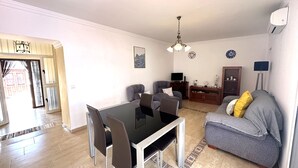 Una sala de estar con una mesa de comedor, sillas, un sofá, un televisor y una lámpara.