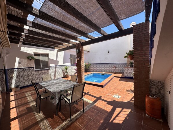 Un pati exterior amb taula i cadires, una piscina i plantes en testos.