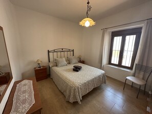 Een slaapkamer met een bed, nachtkastjes, een stoel, een raam met gordijnen en een hanglamp.