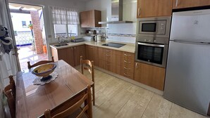 Una cocina con armarios de madera, un refrigerador de acero inoxidable, un horno, un microondas, un lavamanos y una mesa de comedor con sillas.