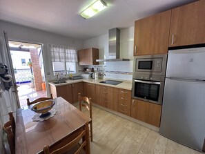 A kitchen with wooden cabinets, a stainless steel refrigerator, an oven, a microwave, a sink, and a dining table with chairs. - R1399, Casa Nina Pariles, Maro (Maro)